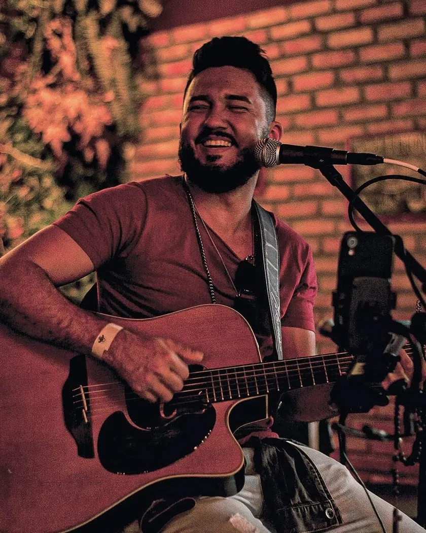 Robson Melo tocando violão e sorrindo no palco